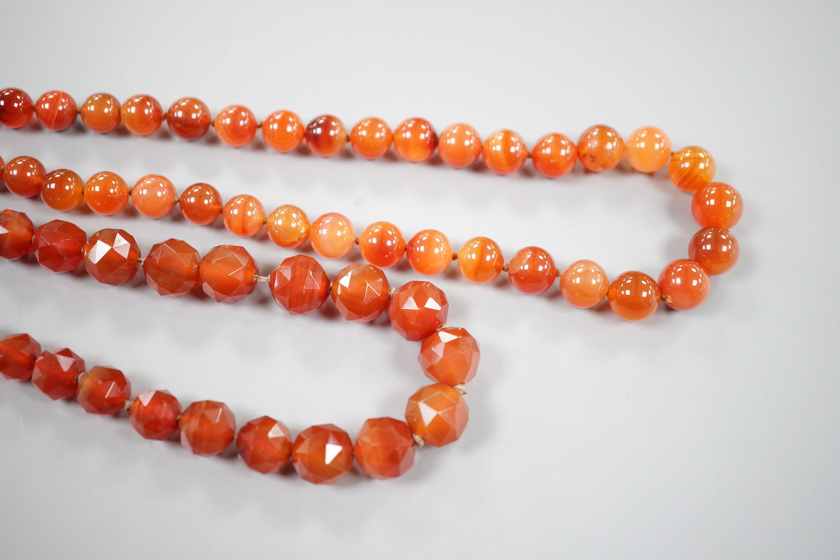 Two single strand carnelian necklace, one with facet cut beads, 44cm & 60cm, both with yellow metal clasps.